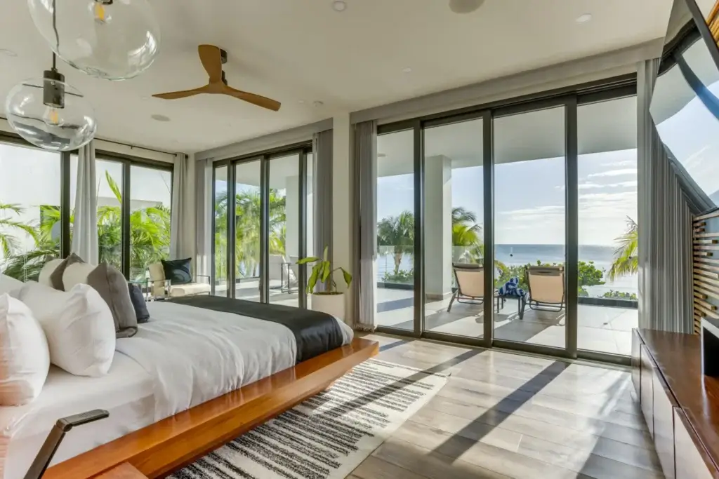 Luxury beachfront villa bedroom with a king bed and open glass doors revealing an intimate ocean view in Belize.
