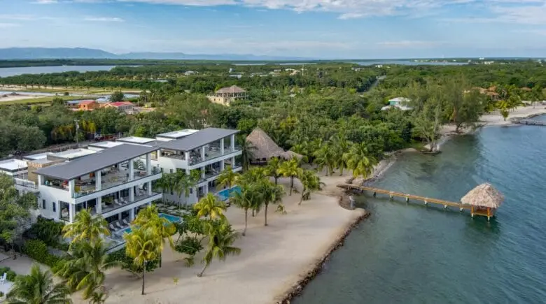 "Aerial drone view of the beach, wooden pier, and luxury resort in Placencia, Belize at sunset.
