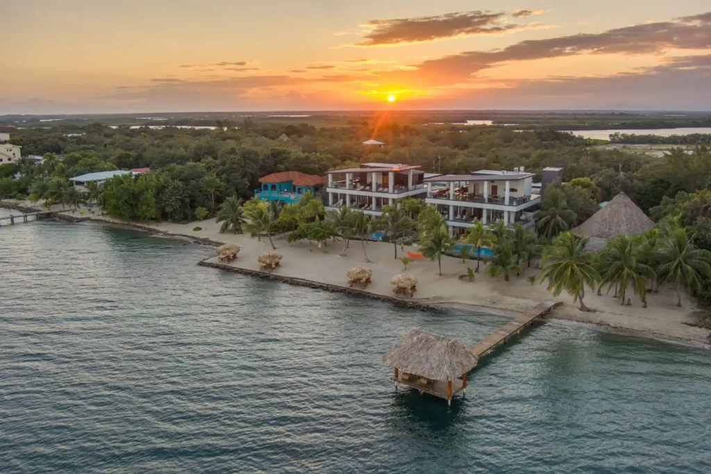 Aerial sunset view of The Villas at Playa de Coco beachfront resort, private pier, and swimming pool in Placencia, Belize