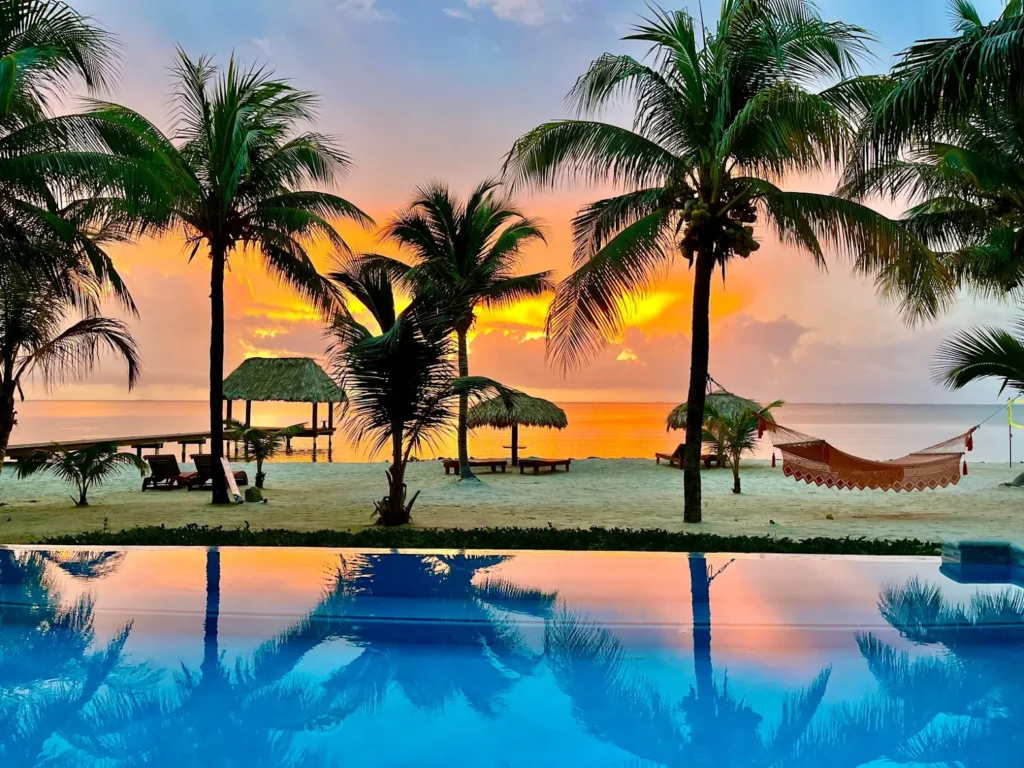 Aerial drone view of the private white-sand beach, wooden pier, and luxury smart villas at The Villas at Playa de Coco in Placencia, Belize at sunset.