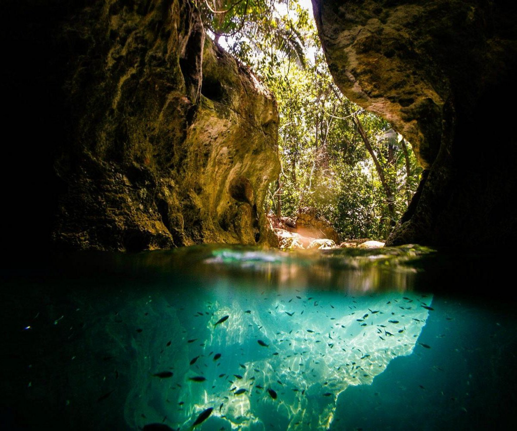 Tour guide and travelers exploring the Actun Tunichil Muknal (ATM) Cave in Belize, illuminating the calcified 'Crystal Maiden' skeletal remains with headlamps.