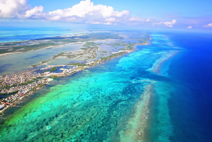 Aerial view of the turquoise coral reef and a wooden overwater pier in Belize.