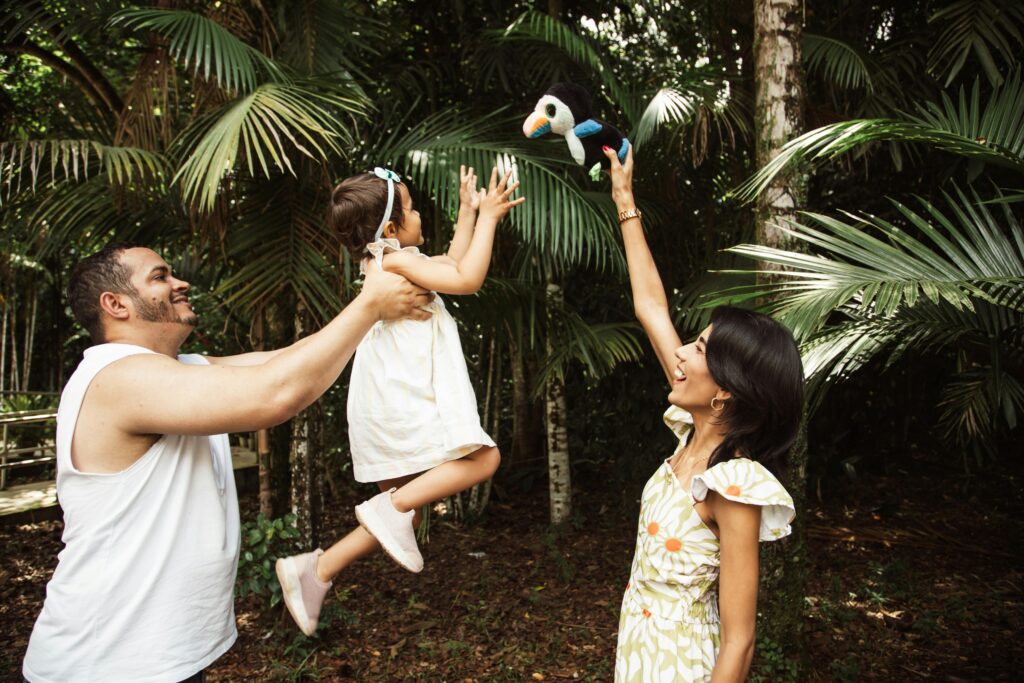 A family enjoying a tropical vacation in Belize, with a father lifting his young child in the air near a scenic waterfront.