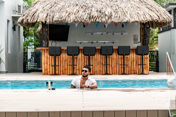 The resort infinity pool at Villas at Playa de Coco with a thatched-roof Tiki Bar in the background, under palm trees in Placencia Belize.