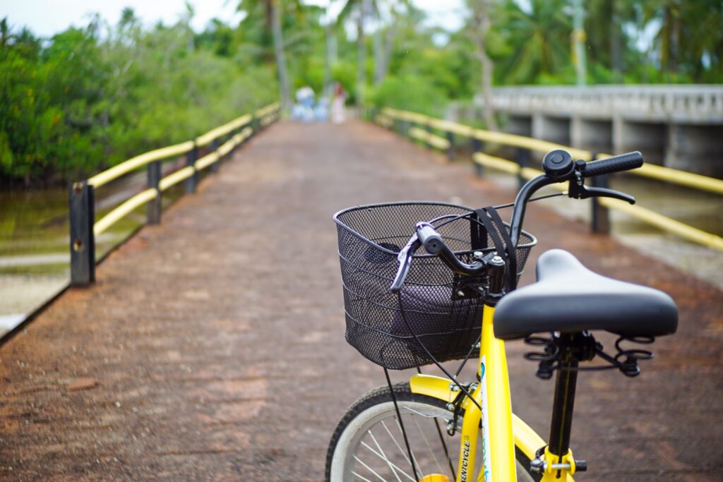 A close-up of a yellow resort bicycle with a front basket, parked on a wooden coastal bridge surrounded by tropical trees at Villas at Playa de Coco.